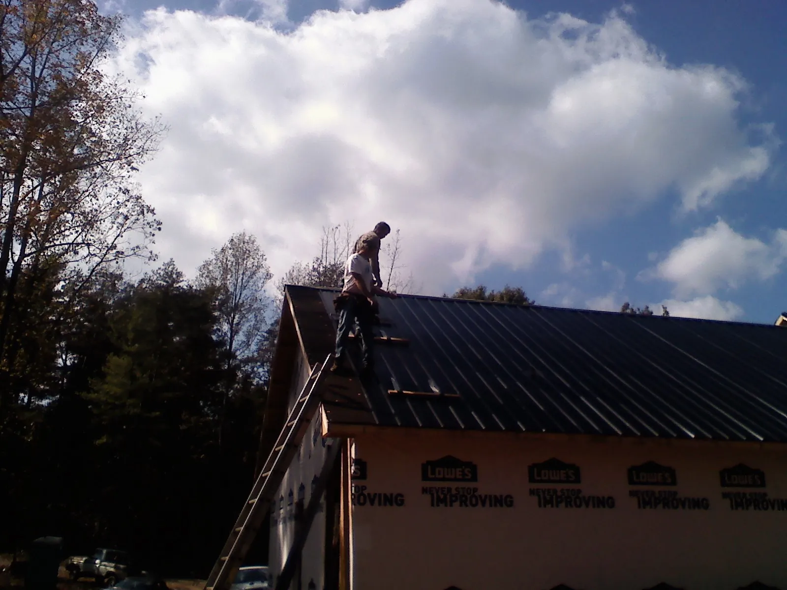 Roofer fastening dark metal panels high against a cloudy sky, from a Roof Inspection job in Seattle