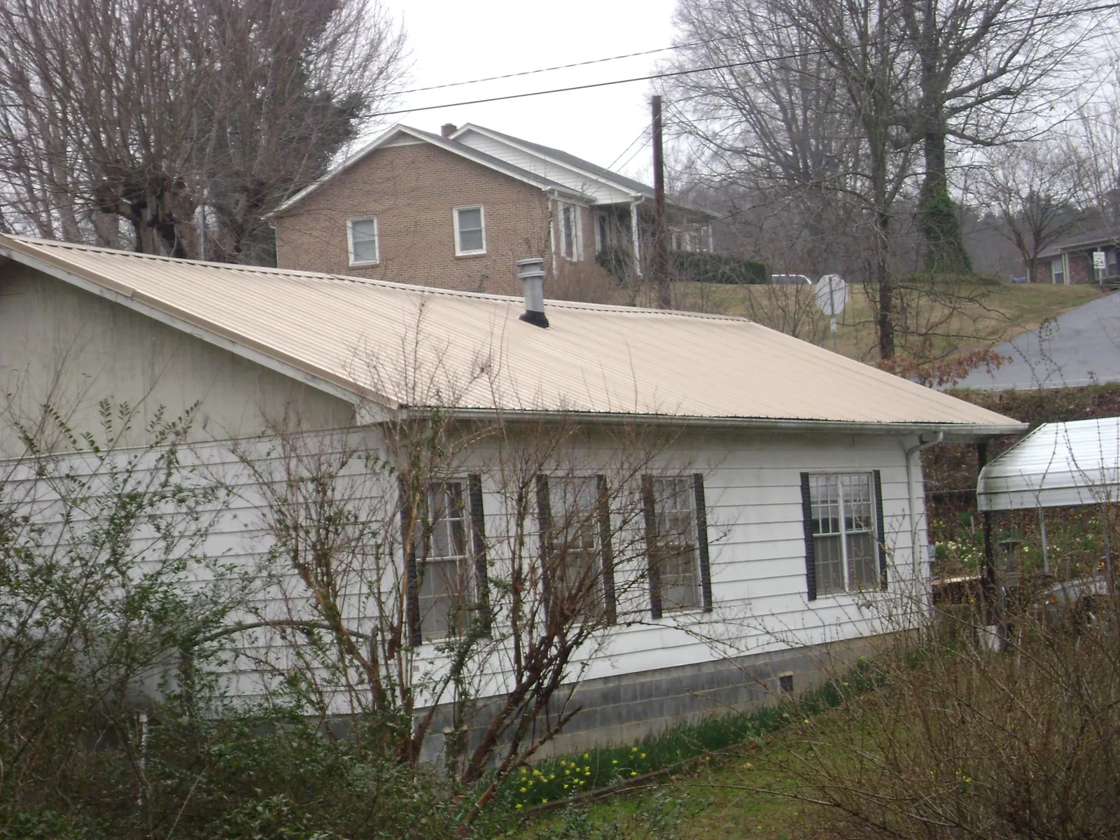 Tan metal roof on a white sided house set into a hillside — Commercial Roofing by Roofing Brothers in Seattle